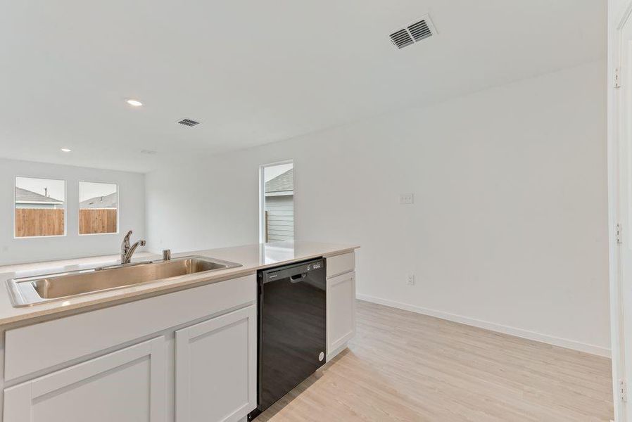 Kitchen with light wood-style flooring, a sink, visible vents, white cabinetry, and black dishwasher