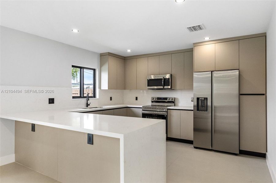 Kitchen featuring flat-panel cabinetry, quartz countertops, tile backsplash, stainless steel appliances, and recessed lighting