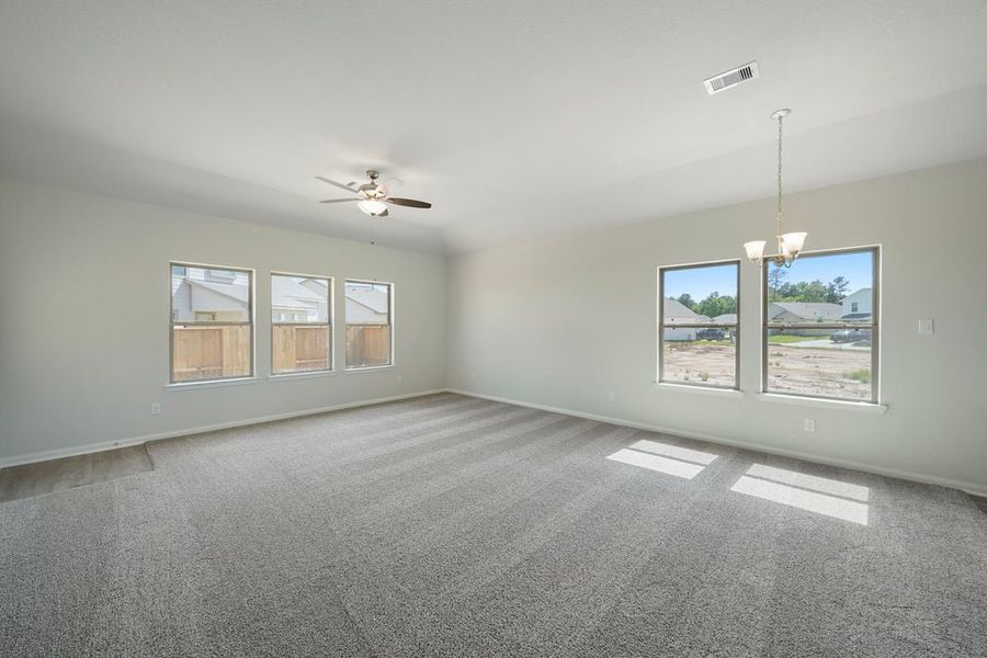 Spacious empty living room with gray carpet, ceiling fan, chandelier, and multiple windows