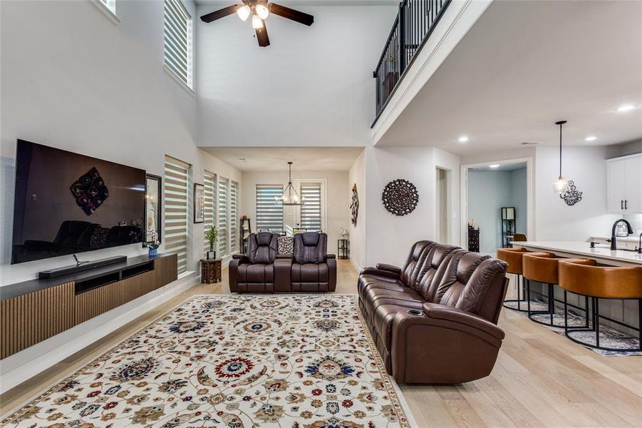 Living room with light wood-style floors, ceiling fan, and a high ceiling
