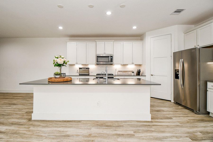 This kitchen features modern white cabinetry, stainless steel appliances, and a spacious island with a sleek countertop, ideal for cooking and entertaining. The wood-style flooring adds warmth and elegance to the space. This kitchen features modern white cabinetry, stainless steel appliances, and a spacious island with a sleek countertop, ideal for cooking and entertaining. The wood-style flooring adds warmth and elegance to the space.