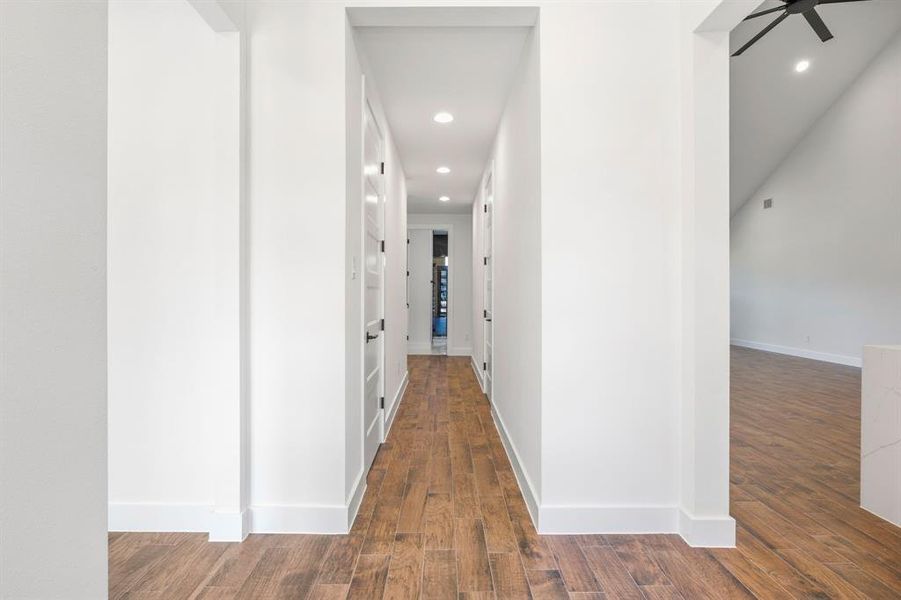 Hallway featuring wood-finish flooring, recessed lighting, and white panel doors with black hardware Hallway featuring wood-finish flooring, recessed lighting, and white panel doors with black hardware