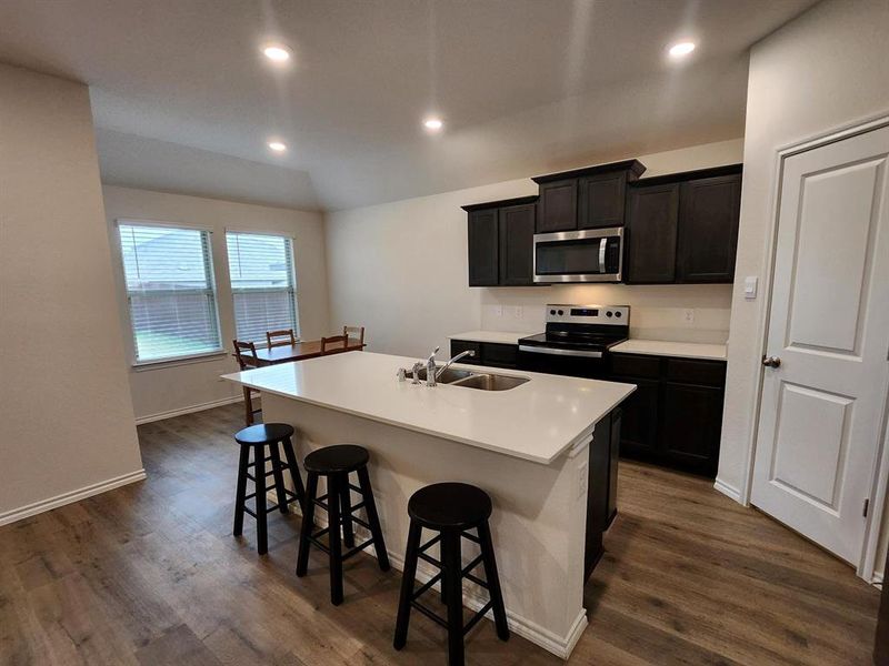 Kitchen featuring range, a center island with sink, a kitchen breakfast bar, recessed lighting, and dark wood-type flooring