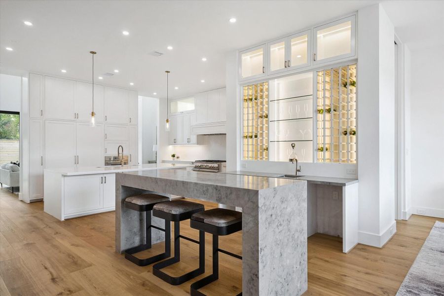 Elegant wet bar with marble waterfall counter, wine storage, and display shelving. Elegant wet bar with marble waterfall counter, wine storage, and display shelving.