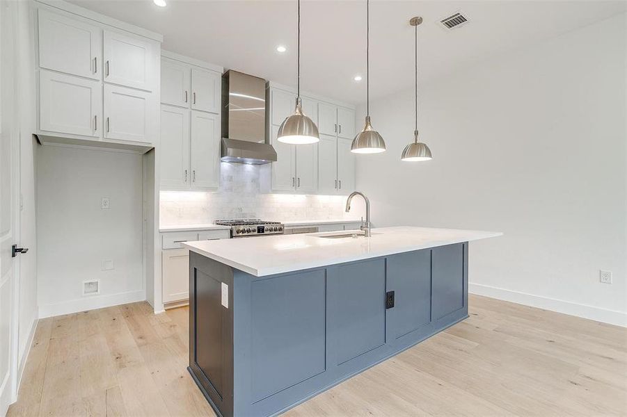 Kitchen featuring wall chimney range hood, decorative backsplash, light wood-style flooring, stove, and a sink