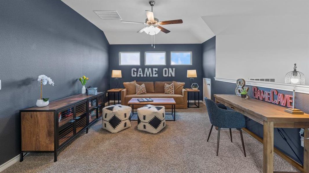 Carpeted bonus room featuring a ceiling fan, three horizontal windows, a built-in wood-finish desk, and a low wall with a white cap Carpeted bonus room featuring a ceiling fan, three horizontal windows, a built-in wood-finish desk, and a low wall with a white cap
