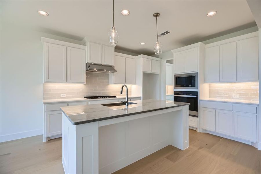 Kitchen with oven, a sink, stainless steel microwave, under cabinet range hood, and tasteful backsplash