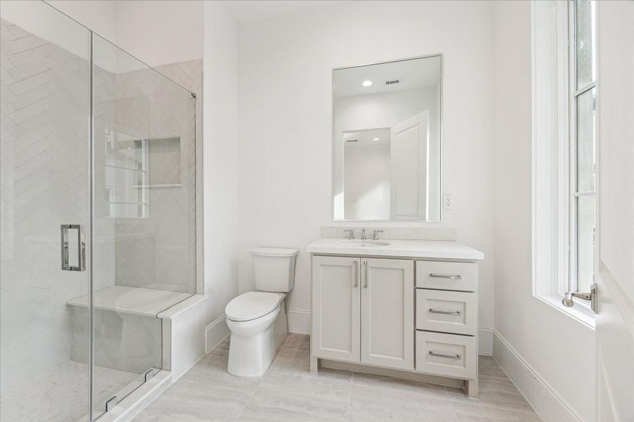 En-suite bath features glass-enclosed freestanding shower lined with Frammenti Bianco Glazed tiles, Quartz countertops, and large vanity area with under-cabinet storage.