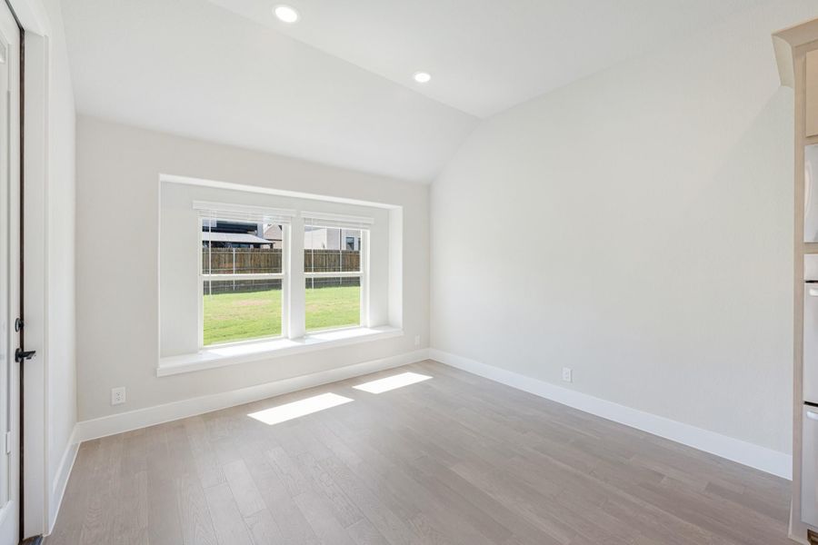 Empty bedroom with light hardwood floors, vaulted ceiling, and a large window overlooking a backyard.