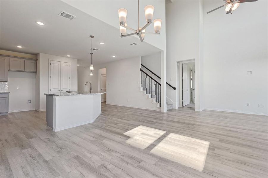 Kitchen featuring an island with sink, light stone countertops, gray cabinetry, light hardwood / wood-style floors, and decorative light fixtures