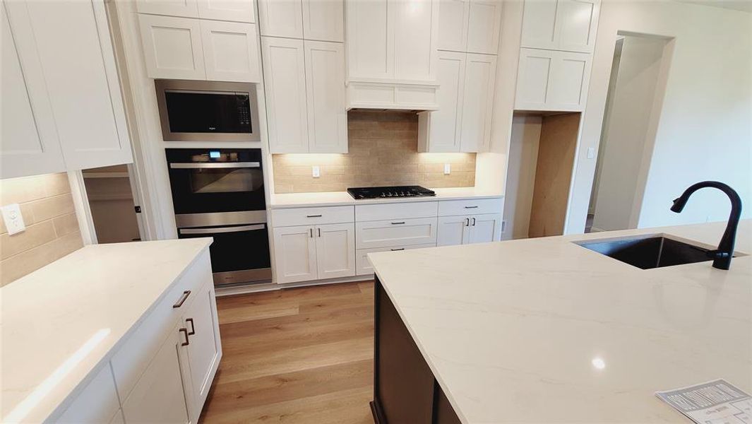 Contemporary kitchen featuring white shaker cabinetry, light wood-finish flooring, and white countertops