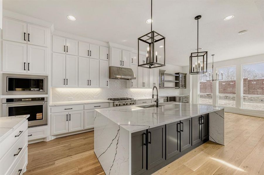Kitchen with light stone countertops, stainless steel appliances, a spacious island, white cabinetry, and light wood-style flooring