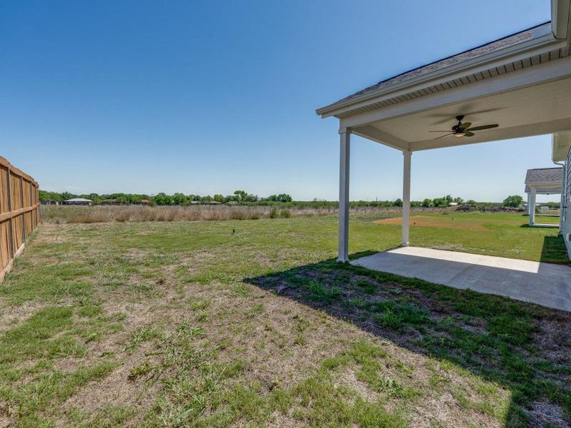 View of yard with a rural view, a ceiling fan, a patio area, and fence