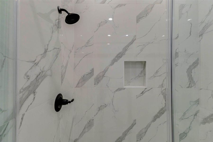 Sleek walk-in shower with dramatic marble-look wall tile, glass enclosure, matte black shower fixtures, and a built-in recessed niche for storage. The clean lines, glossy finish, and contemporary black accents give the bath a spa-like feel with a modern luxury look.