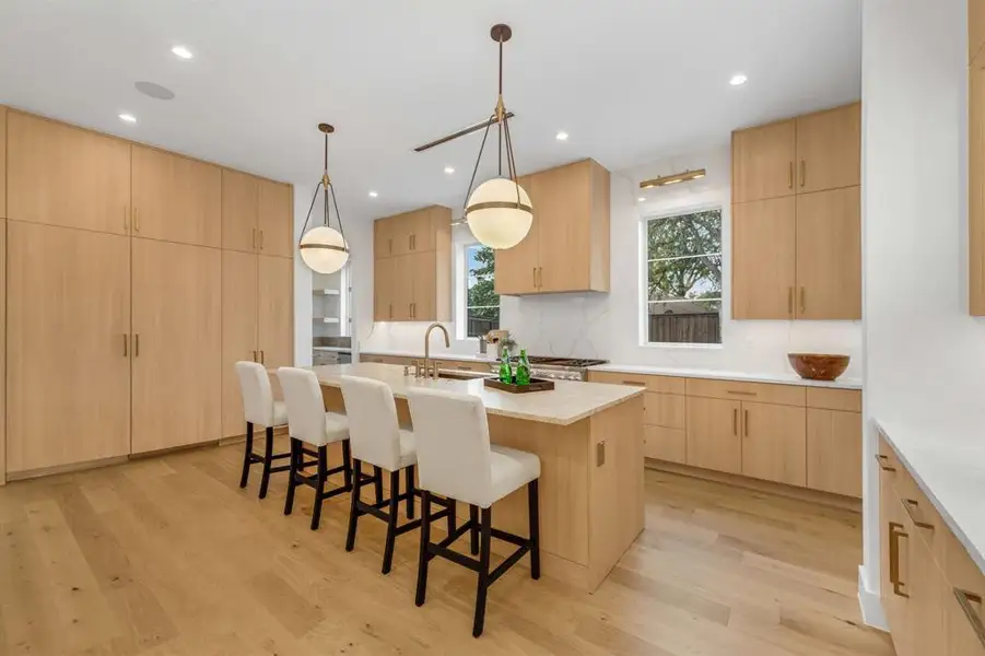 Kitchen with hanging light fixtures, light stone counters, a breakfast bar area, light brown cabinets, and modern cabinets