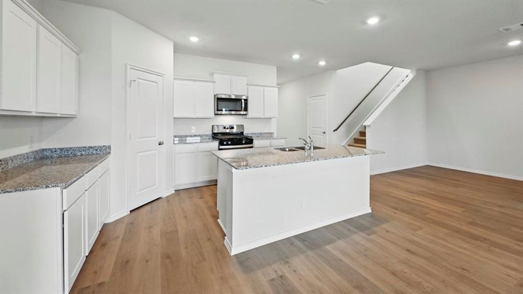 Kitchen featuring an island with sink, white cabinetry, light stone counters, stainless steel appliances, and light wood-style flooring