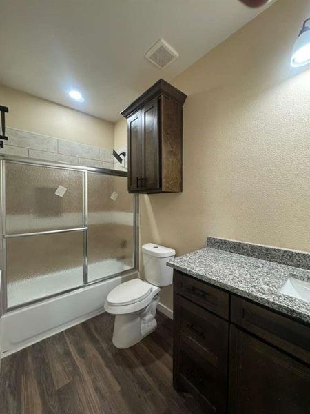 Full bath featuring dark wood-type flooring, vanity, combined bath / shower with glass door, recessed lighting, and a textured wall