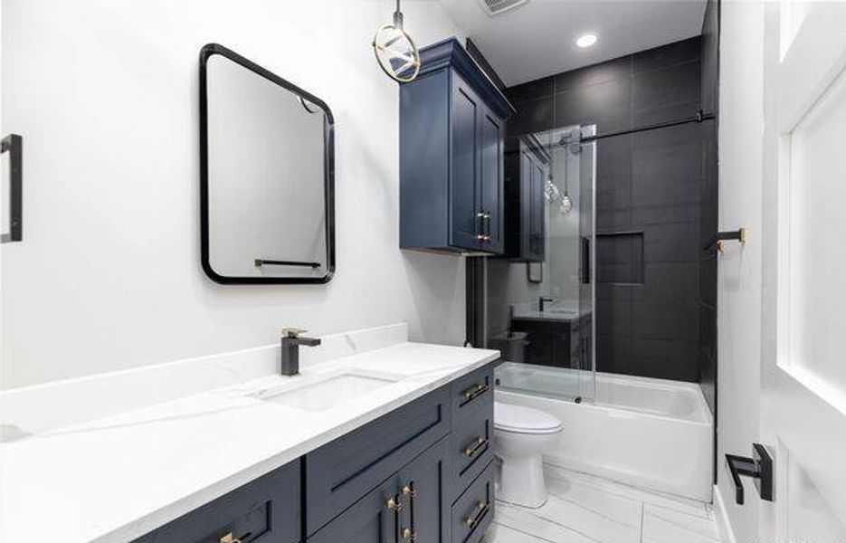 Modern bathroom featuring a dark blue vanity with gold-tone hardware, a white countertop with an integrated sink, and a sleek black framed mirror
