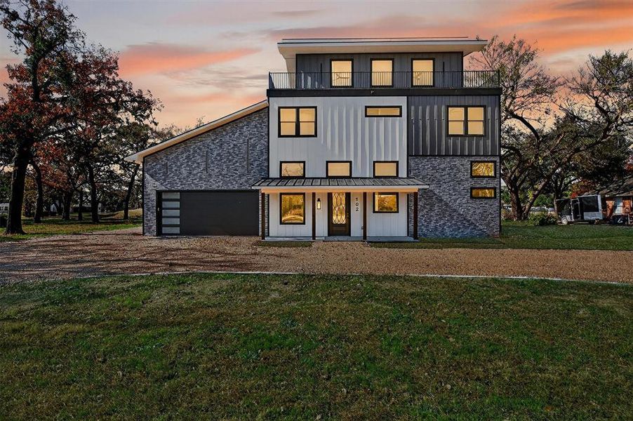 Back of property at dusk featuring board and batten siding, a lawn, driveway, and stone siding