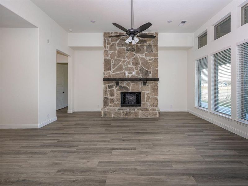 Unfurnished living room featuring ceiling fan, wood finished floors, and a stone fireplace Unfurnished living room featuring ceiling fan, wood finished floors, and a stone fireplace