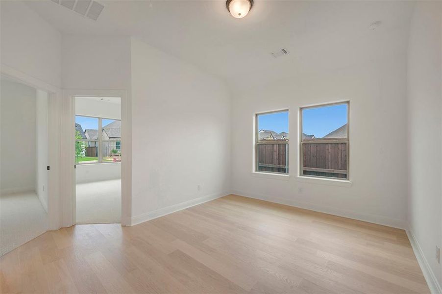 Spacious room with light wood-finish flooring, white walls, and a semi-flush mount ceiling light