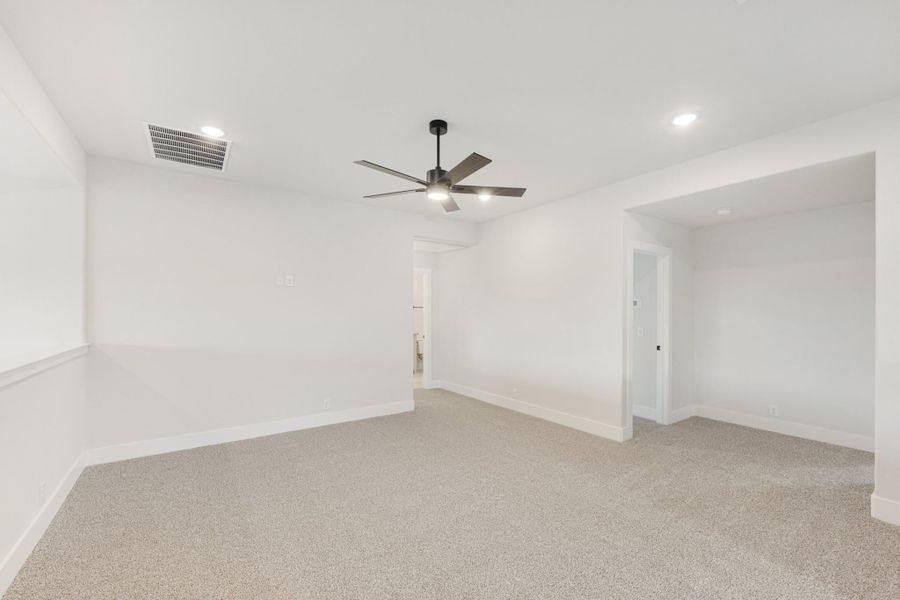 Empty bedroom with gray carpet, white walls, and a ceiling fan with light fixture