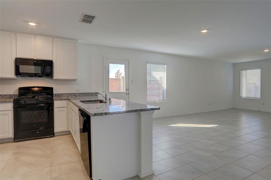 Kitchen featuring recessed lighting, black appliances, light tile patterned floors, light stone counters, and a peninsula