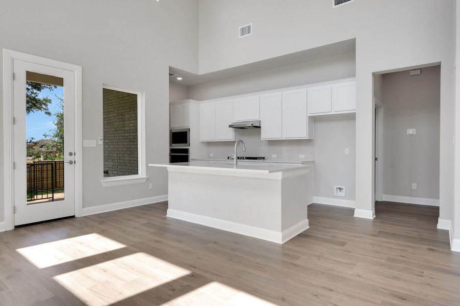 Kitchen featuring white cabinets, light countertops, light wood-type flooring, an island with sink, and a high ceiling