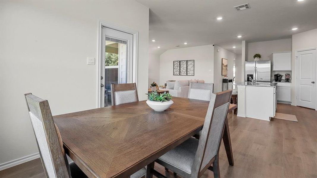The dining area features a wooden table and cushioned chairs, with a view of the kitchen and living room