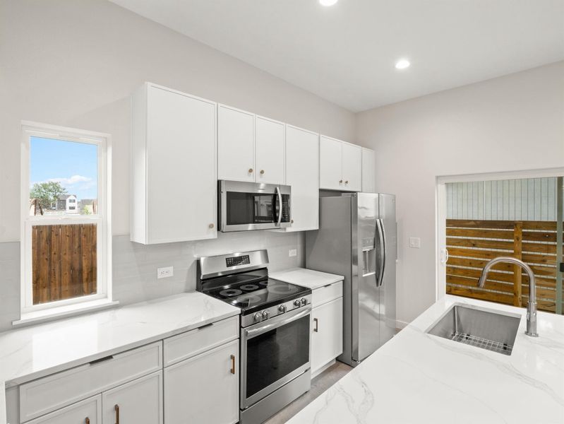 Kitchen featuring white cabinetry, stainless steel appliances, white countertops with veining, an undermount sink with a gooseneck faucet, and a sliding glass door