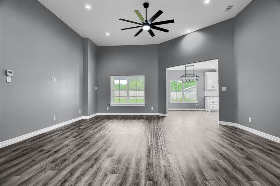 Empty room featuring dark hardwood / wood-style flooring, a high ceiling, and ceiling fan with notable chandelier