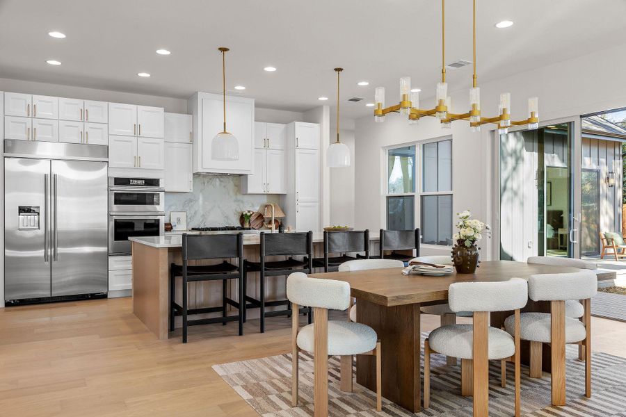 Kitchen with stainless steel appliances, hanging light fixtures, light wood-style flooring, backsplash, and a breakfast bar area