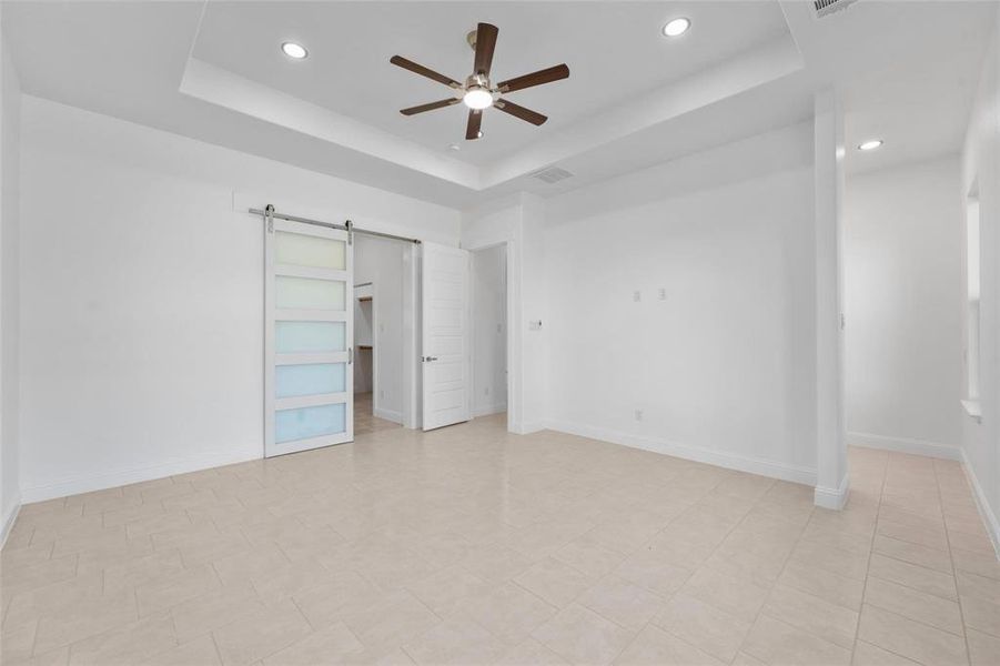 Unfurnished bedroom with a raised ceiling, a barn door, recessed lighting, and ceiling fan Unfurnished bedroom with a raised ceiling, a barn door, recessed lighting, and ceiling fan