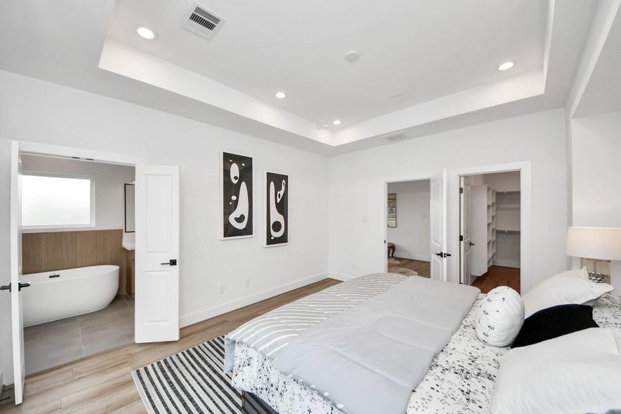Experience luxury in this spacious primary bedroom featuring elegant tray ceilings, modern recessed lighting, and seamless access to a chic ensuite bathroom and expansive walk-in closet.