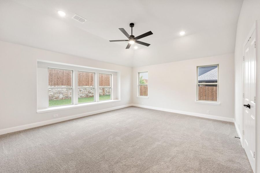 Empty bedroom with gray carpet, black ceiling fan, and multiple windows overlooking backyard Empty bedroom with gray carpet, black ceiling fan, and multiple windows overlooking backyard