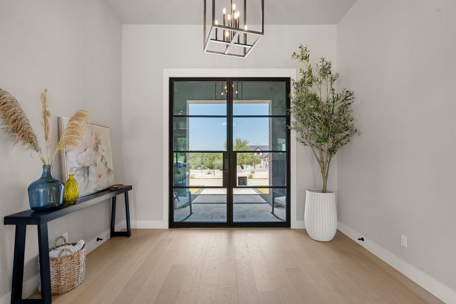 Double glass doors framed in black open into a welcoming foyer with hardwood flooring.