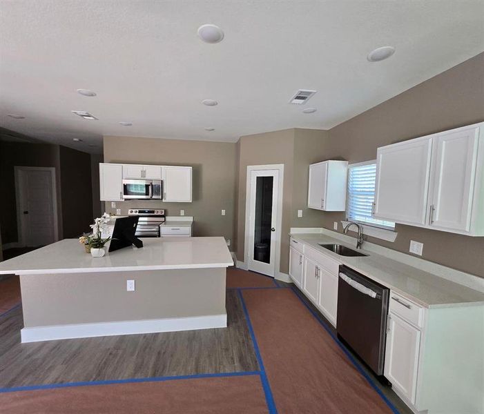 Open-concept kitchen featuring an expansive central island with a solid surface countertop, white shaker cabinetry, stainless steel appliances, and recessed lighting