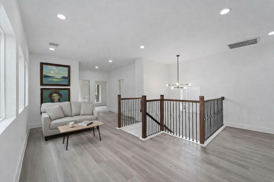 This open upstairs space features light-colored wood-look laminate flooring and white walls with multiple recessed ceiling lights, the landing providing access to other rooms.