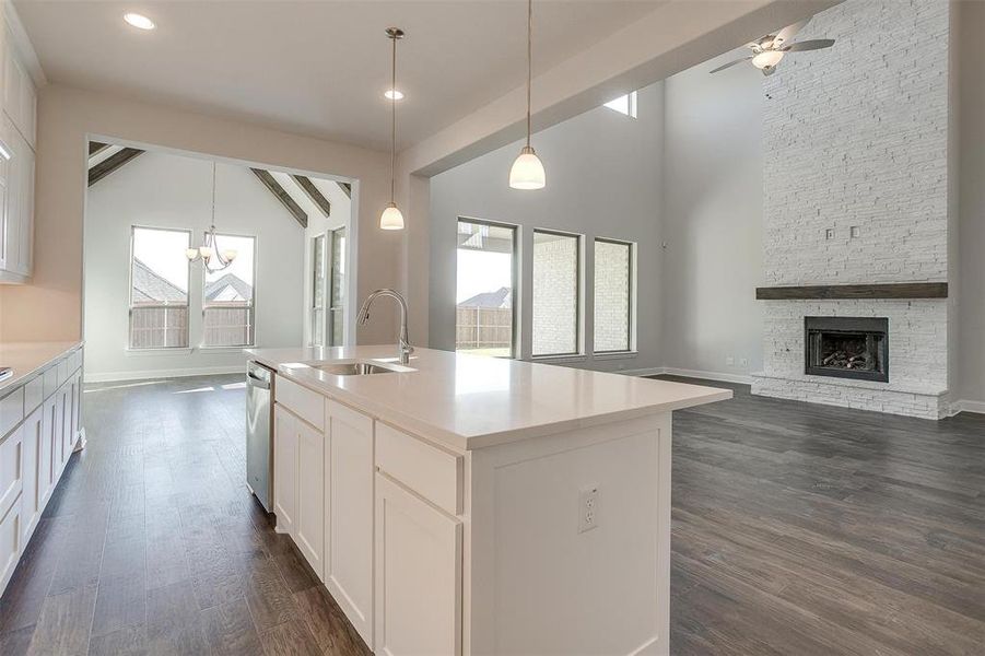 Kitchen with beamed ceiling, sink, an island with sink, ceiling fan with notable chandelier, and a fireplace