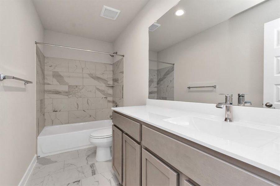 Indulge in refined charm in the secondary bathroom, where the tile flooring harmonizes with a bath/shower combo surrounded by tasteful tile. Light wood cabinets, coupled with a gorgeous countertop, elevate the space, cultivating a truly welcoming atmosphere. Sample photo of completed home with similar floor plan. As-built interior colors and selections may vary.