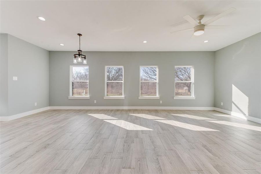 Unfurnished room with ceiling fan with notable chandelier and light hardwood / wood-style flooring