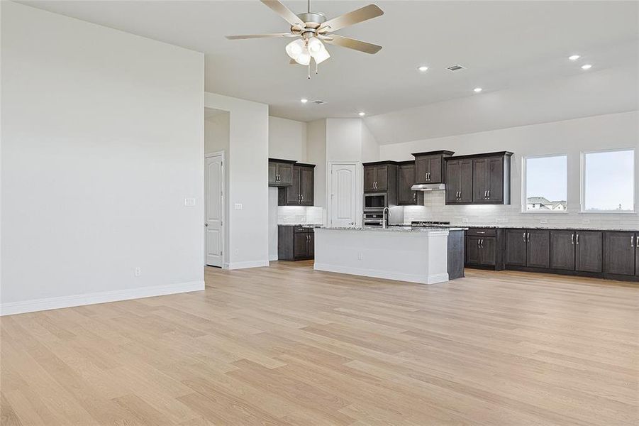 Kitchen with tasteful backsplash, stainless steel appliances, a kitchen island with sink, ceiling fan, and light hardwood / wood-style flooring