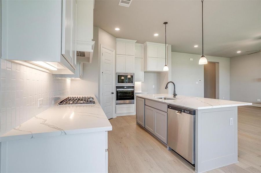 Kitchen with light hardwood / wood-style floors, stainless steel appliances, decorative light fixtures, a kitchen island with sink, and sink