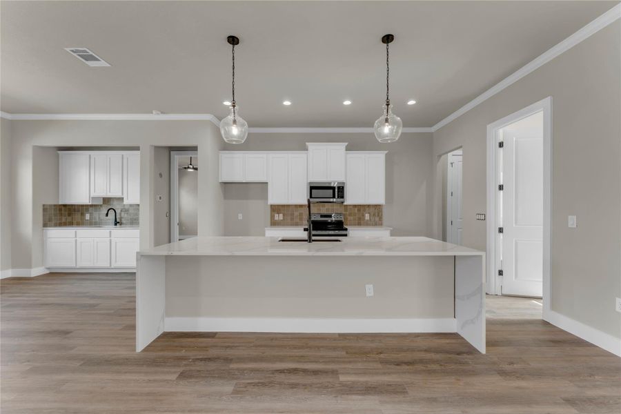 Kitchen with backsplash, white cabinetry, a large island, light stone counters, and stainless steel appliances