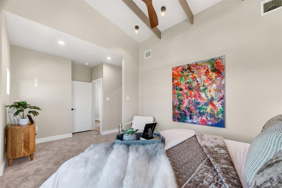 A third view of the primary suite showcases the full sweep of the sloped beamed ceiling from a wider angle. The room's generous footprint accommodates a king-sized layout with room to spare, a standout feature in this urban new construction.