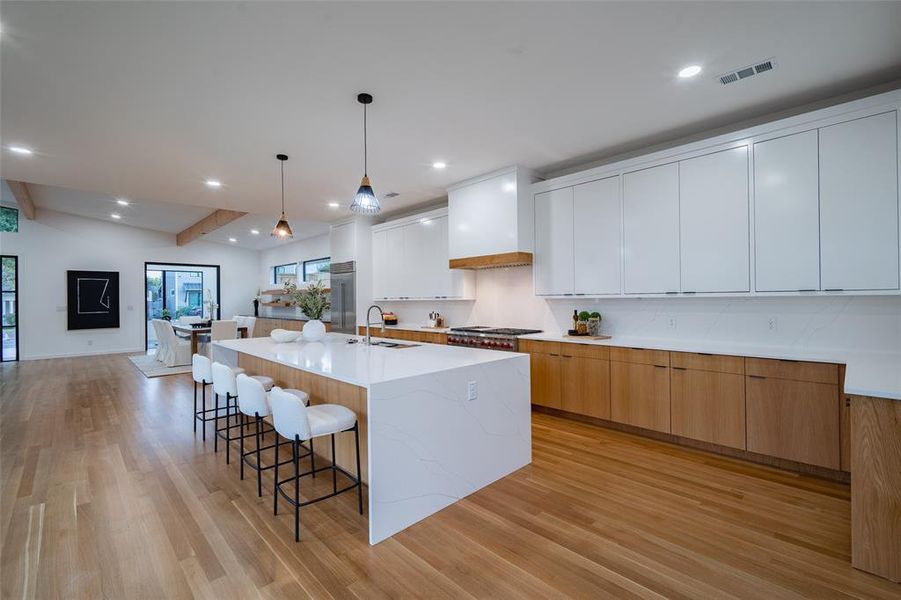 Kitchen featuring sink, a large island, pendant lighting, white cabinetry, and light hardwood / wood-style flooring