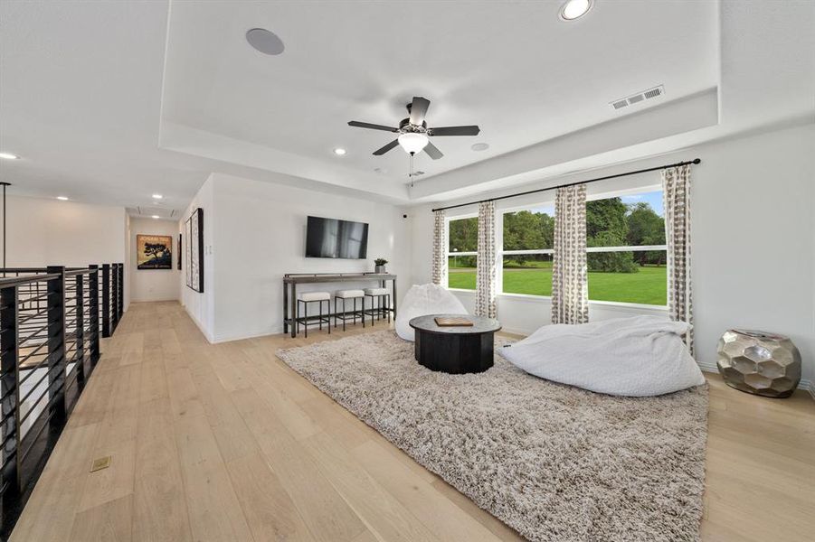 Game room with light hardwood / wood-style floors, a tray ceiling, and ceiling fan