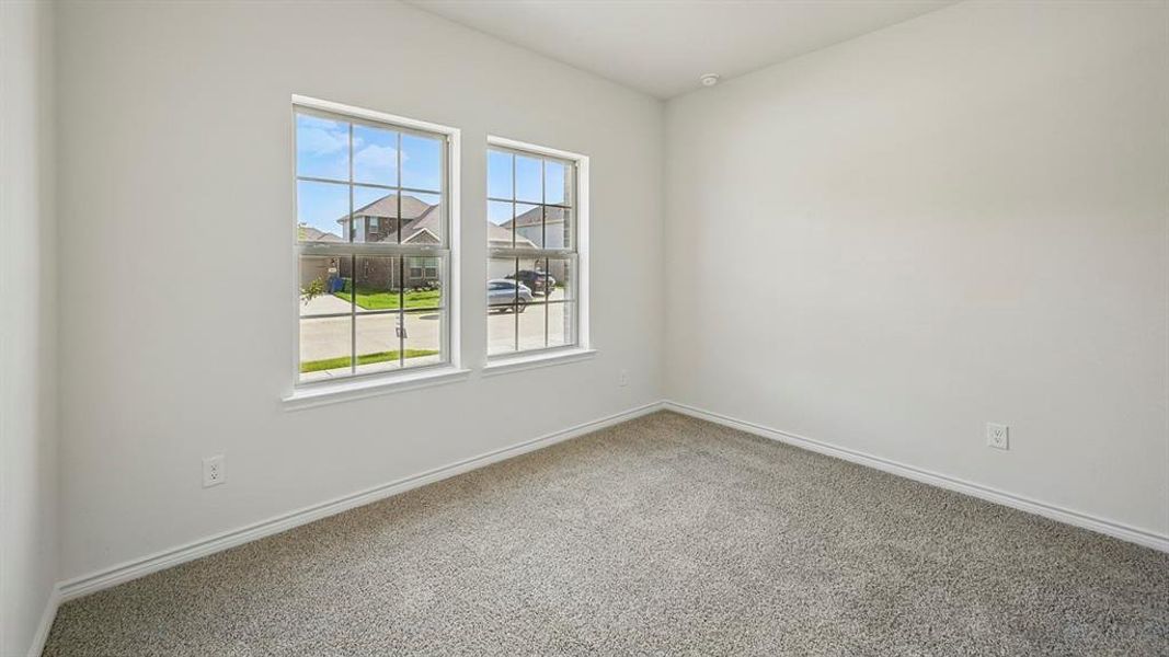 Bright interior space featuring two large windows with grid accents, light grey carpeting, white baseboards, and neutral wall tones Bright interior space featuring two large windows with grid accents, light grey carpeting, white baseboards, and neutral wall tones