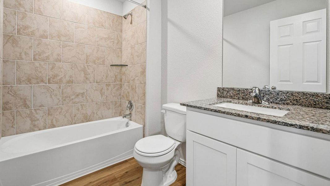 Modern bathroom featuring elegant granite counters and a tiled shower-over-tub.