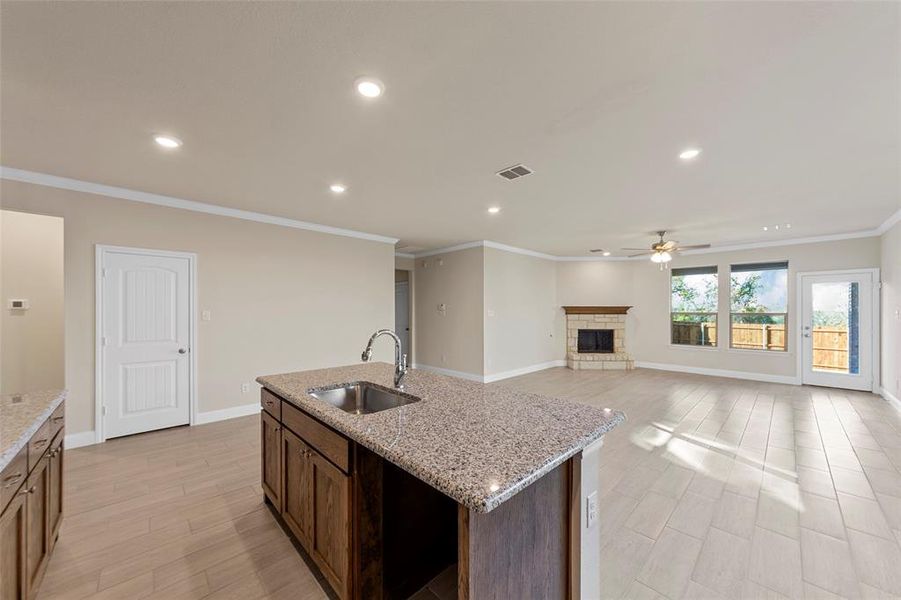 Kitchen with ceiling fan, sink, light stone counters, a fireplace, and a center island with sink